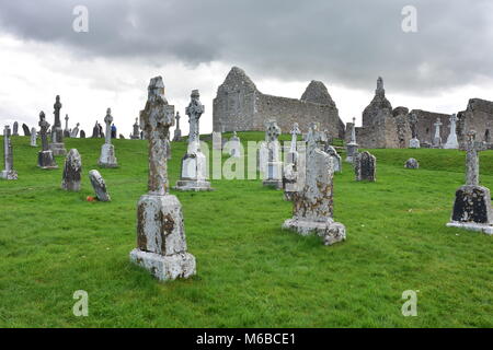 Ancient cemetery with weathered stone Celtic crosses and medieval church ruins in background on grounds of monastery in Clonmacnoise in Ireland. Stock Photo