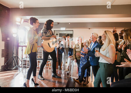 Wedding guests are enjoying some acoustic entertainment. There is a man playing guitar and a woman singing and everyone is dancing along. Stock Photo