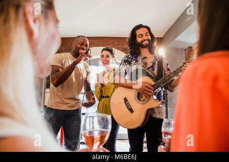 Two young men and a young woman are singing and playing guitar at an entertainment venue to a crowd. Stock Photo