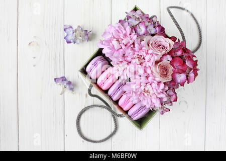 Gift set: box with flowers (hydrangea, rose, chrysanthemum) and macaroni on a wooden background. Selective focus, top view. Stock Photo