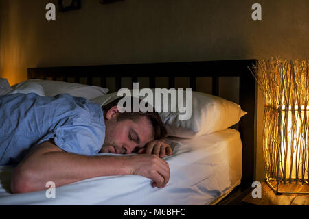 Portrait of young caucasian tired man laying on bed using laptop for a long time. Stock Photo