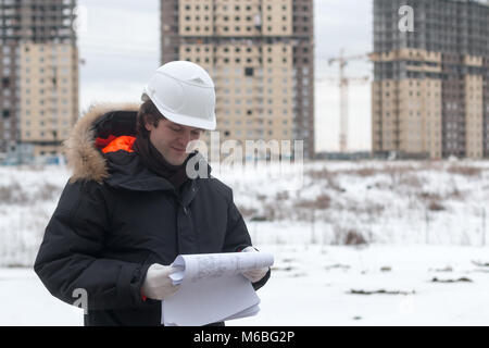 Worker or engineer holding drawing in hands and reading it on background of new apartment buildings and construction cranes on background.Architect en Stock Photo