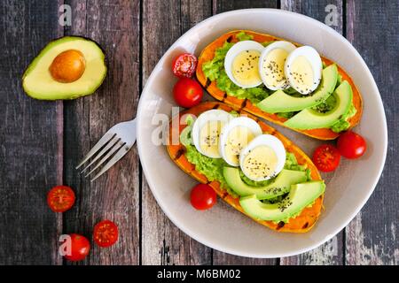Sweet potato toasts with avocado, eggs and chia seeds on a plate. Top view on a dark wood background. Stock Photo