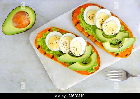 Sweet potato toasts with avocado, eggs and chia seeds on a marble server. Top view on a bright background. Stock Photo