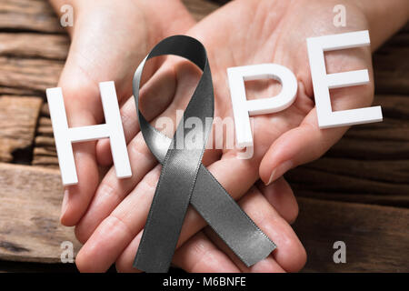 Person's Hand Showing Ribbon With Hope Text To Support Brain Cancer Awareness