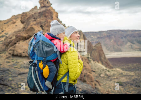 Family hike baby boy travelling in mother's backpack. Hiking adventure with child on autumn family trip in mountains. Vacations journey with infant ca Stock Photo