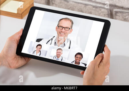 A Person Videoconferencing With Smiling Male And Female Doctors On Digital Tablet Stock Photo