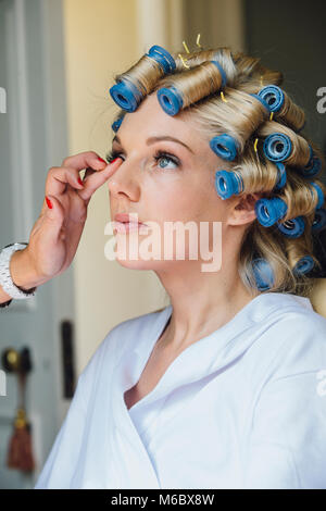 Beautiful bride is having a makeover on her wedding day. She has rollers in her hair and someone is applying product to her face. Stock Photo