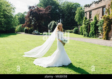 Beautiful bride is posing for the camera in her wedding dress in a formal garden. Stock Photo