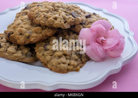 Closeup on stack of chocolate Chip and Oatmeal Cookies in white plate on pink background and decorated with pink flower- cookies for mom on mothers da Stock Photo
