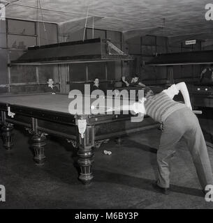 1960s, historical, young men playing a game of snooker in a snooker hall, with a young man with rolled-up shirt sleeves and a tank-top positioned at the table about to strike a ball, England, UK. Snooker was a popular leisure game or pasttime in this era, with many tables to play at lunchtime or early evening after work. The game originated among Brtish Army officers stationed in India in the late 19th century. Stock Photo