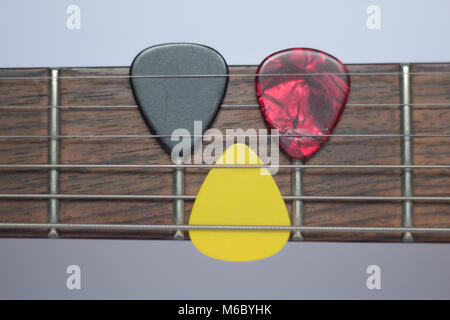 Guitar picks on a rosewood electric guitar neck, white background. Stock Photo