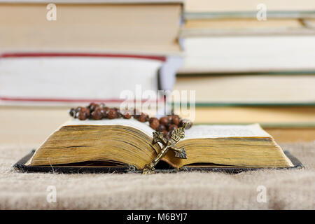 An open old book with a rosary in a hard cover with blurred books in the background Stock Photo