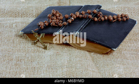 An open old book with a rosary in a hard cover lying on the jute Stock Photo