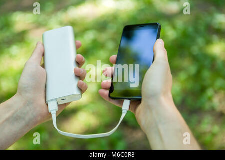 Image of man holding phone and powerbank in street on summer day Stock Photo
