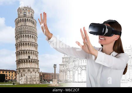 Smiling Young Woman Wearing Virtual Reality Glasses Trying To Touch Leaning Tower Of Pisa Stock Photo