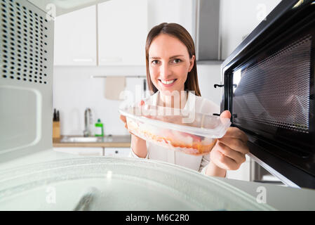 Young Woman Preparing Food In Microwave Oven At Kitchen Stock Photo