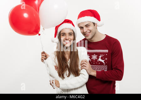 Christmas Concept - Young girlfriend holding balloon is hugging and playing with her boyfriend doing a surprise on Christmas Stock Photo