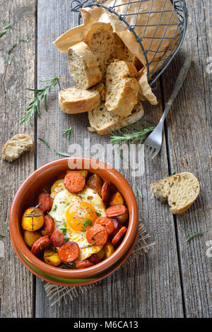 Spanish tapa: Spicy chorizo sausage with fried egg and baby potatoes served in a terra cotta cazuela dish Stock Photo
