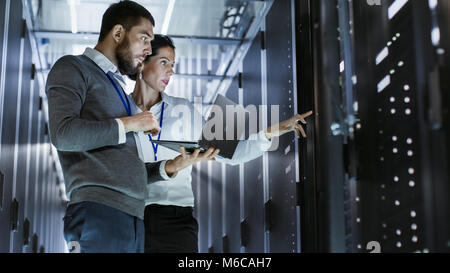Male IT Specialist Holds Laptop and Discusses Work with Female Server Technician. They're Standing in Data Center, Rack Server Cabinet is Open. Stock Photo