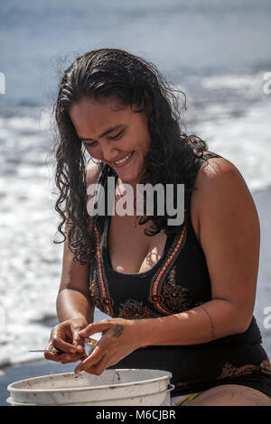 Woman, Polynesian, laughs, cleans fish on the beach, swimsuit, Tahiti, French Polynesia Stock Photo