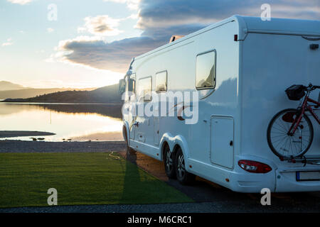 Large camper Van parking near the water at a campsite for motorhomes. Its sunset and the water is calm.