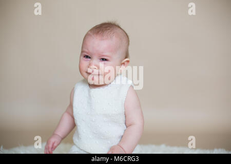 Close portrait of cute little baby boy, isolated on beige background, baby making different facial expressions, crying, sad, smiling, laughing Stock Photo