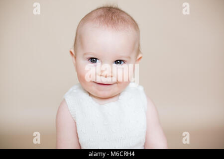 Close portrait of cute little baby boy, isolated on beige background, baby making different facial expressions, crying, sad, smiling, laughing Stock Photo
