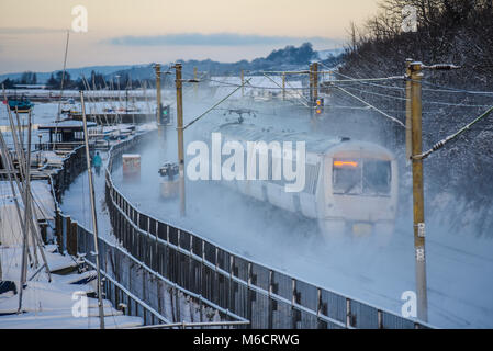 C2C railway train passing at speed through snow covered lines throwing up clouds of snow. Stock Photo