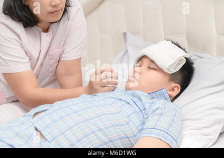 Mother measuring temperature of her ill kid. Sick child with high fever laying in bed and mother holding thermometer, Healthy care concept Stock Photo