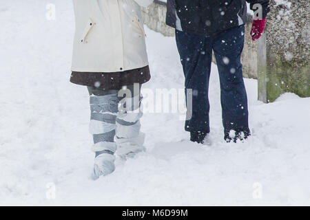 Celbridge, Kildare, Ireland. 02 Mar 2018: Couple out walking through the snow with plastic bags wrapped around legs as an alternative to snow boots. Roads in Celbridge covered in snow in the aftermath of the cold wave bugged 'The Beast from The East' followed by Storm Emma. Winter scenery. Stock Photo