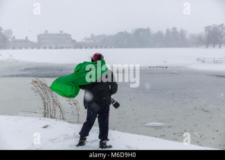 Celbridge, Kildare, Ireland. 02 Mar 2018: Man photographer with Canon equipment taking photos of mallard ducks standing on a frozen pond at the covered in snow Castletown Park in Celbridge. Beast from the east followed by Storm Emma brought snow and high winds paralyzing the country   and forcing Met Éireann to issue the red warning alert across Ireland. Stock Photo