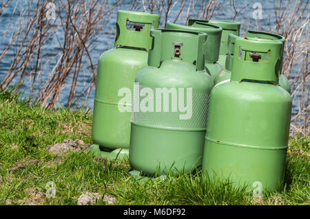 four propane storage bottles standing on a field near the water Stock Photo