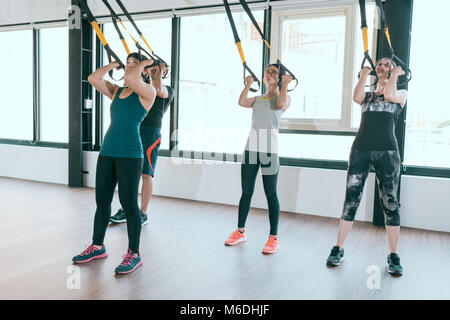 team of fitness TRX suspension straps training exercises Asian people doing the pull up, working with own weight at the gym. Stock Photo