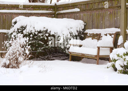 Deep snow on a wooden bench and shrubs and plants in a country garden Stock Photo