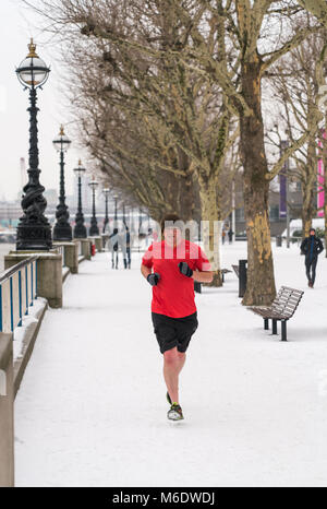 01 March 2018 - London, England. A man wearing shorts, running on the snow, down the embankment in cold weather. Stock Photo