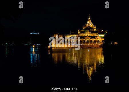 Karaweik Palace hall barge, lit up golden bright at night reflecting on Kandawgyi Lake, Yangon, Myanmar, Burma, Asia. Traditional floating restaurant. Stock Photo