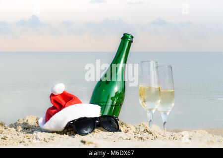 Sparkling wine drink, santa claus hat, sunglasses at seaside symbolising celebration of new year in hot climate or weather Stock Photo