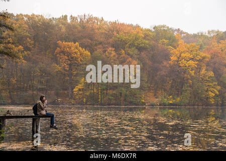 Girl enjoys rest and drinks coffee near the lake at nature park on gold mellow autumn day Stock Photo