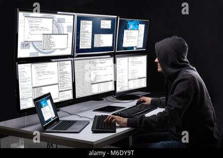 Rear View Of A Hacker Using Multiple Computers For Stealing Data In Office Stock Photo