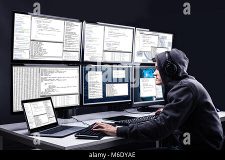Rear View Of A Hacker Using Multiple Computers For Stealing Data In Office Stock Photo