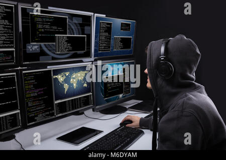 Rear View Of A Hacker Using Multiple Computers For Stealing Data In Office Stock Photo