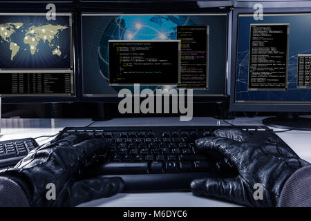 Hacker Wearing Gloves Typing Code On Keyboard In Front Of Multiple Computers Stock Photo