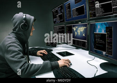 Rear View Of A Hacker Using Multiple Computers For Stealing Data In Office Stock Photo