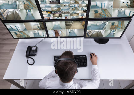 Elevated View Of Male Security Guard Monitoring Multiple Camera Footage On Computer At Workplace Stock Photo