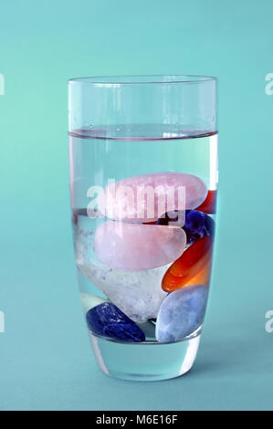 different kinds of crystals in full filled glass of water, on green-blue background, making elixir Stock Photo