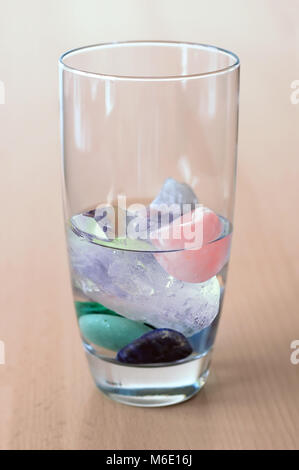 different kinds of gemstones in glass of water, on wooden table, making elixir Stock Photo