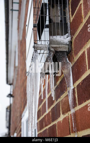 Icicles hang from the outside metal cover over a flue from a gas boiler. Stock Photo