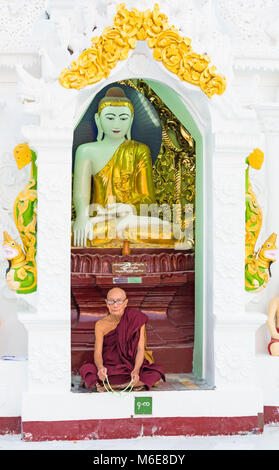 Buddhist monk sitting in front of Buddha shrine at Shwedagon Pagoda, Yangon, Myanmar (Burma), Asia in February Stock Photo
