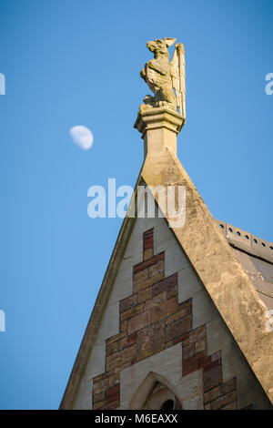 A sculptural finial in the shape of a Griffin (with dog-like attributes) on a Victorian building at Clifton College, Bristol, with moon alongside. Stock Photo